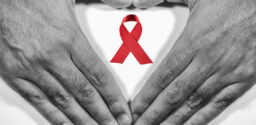 Man forming a heart with his hands and a red ribbon for the fight against AIDS on a white background.