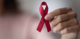 Close up focus on red ribbon in female hands, woman standing indoor promote annual regular health check up, support people with chronic disease, social AIDS campaign, HIV awareness, healthcare concept