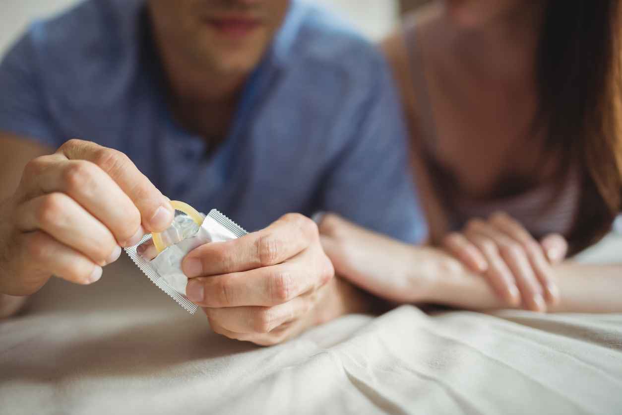 Close-up of couple with a condom on bed in the bedroom, reducing the risk of HIV transmission