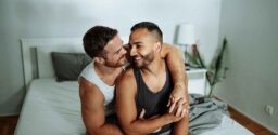 Gay couple smiling and holding hands in bedroom; Tips for Improving Sexual Health