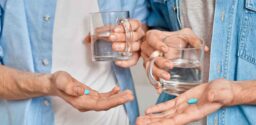 Cropped view of gay couple holding mug with water and pre exposure HIV protection pills in hands, care about health and wellness