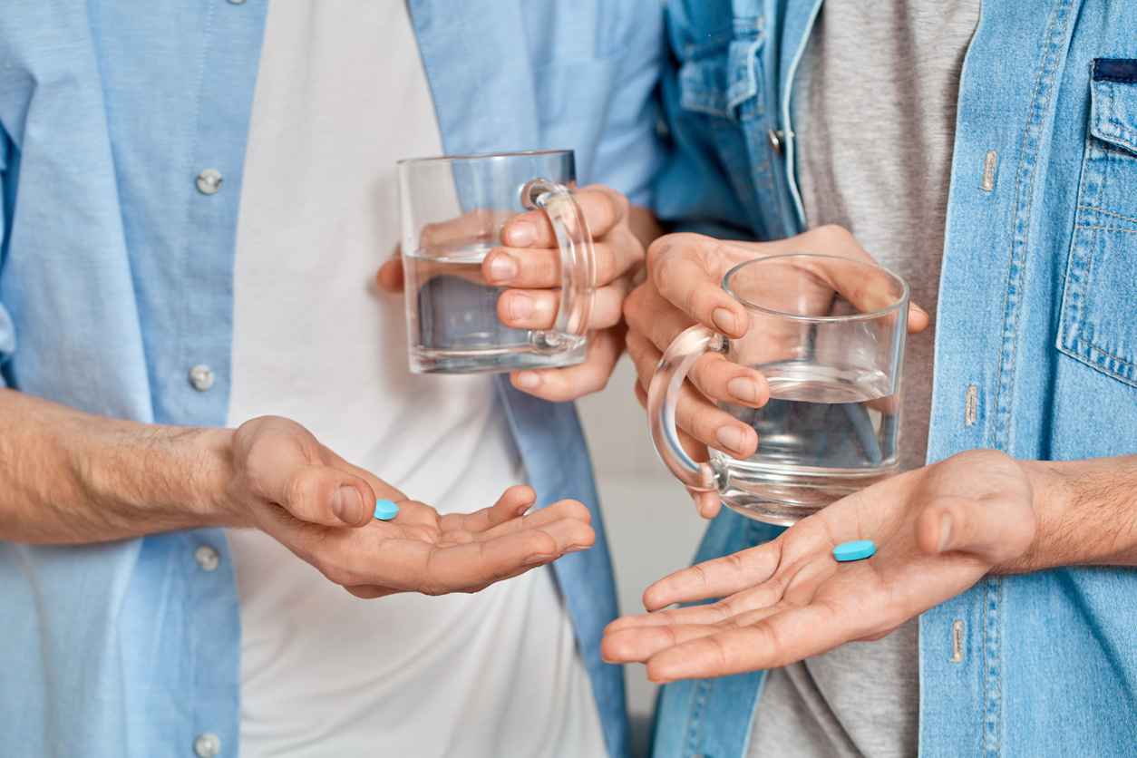 Cropped view of gay couple holding mug with water and pre exposure HIV protection pills in hands, care about health and wellness