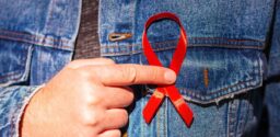 Man wearing Denim Jacket holding a red AIDS awareness ribbon on his chest. World Aids Day. Concept of HIV/AIDS healthcare and medicine.