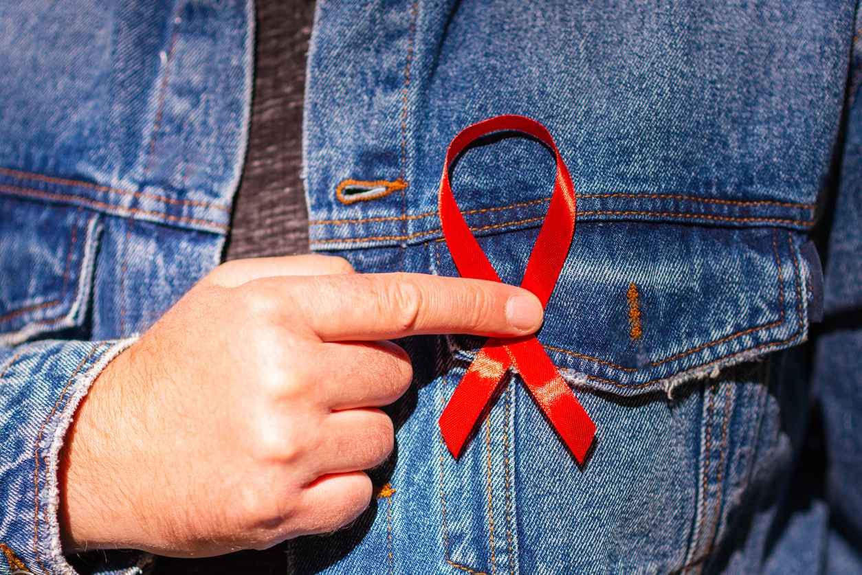 Man wearing Denim Jacket holding a red AIDS awareness ribbon on his chest. World Aids Day. Concept of HIV/AIDS healthcare and medicine.