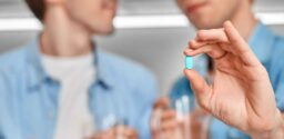 Young gay couple at home standing while holding cups of water and blue pill pre-exposure prophylaxis close-up