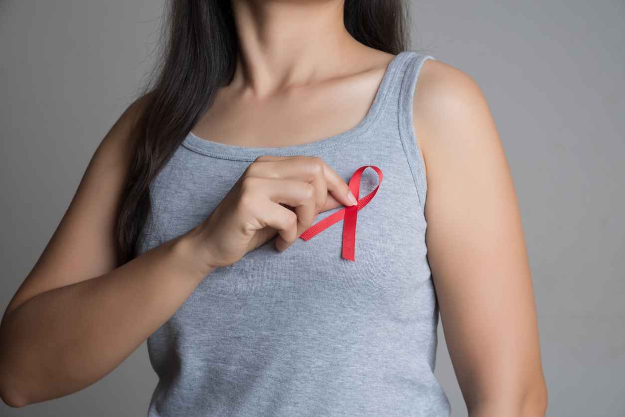 Closeup woman hand holding red ribbon HIV, world AIDS day awareness ribbon; HIV/AIDS and Women's Health