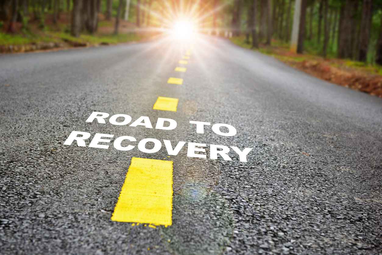 "Road to recovery" written on a road with sunbeams in the distance