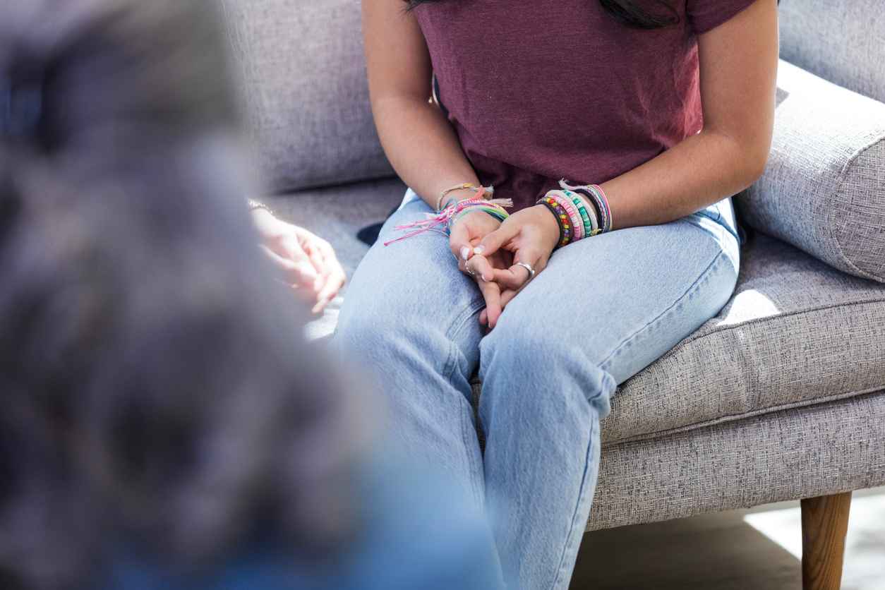 The unrecognizable emotionally stressed young adult woman attends counseling with her unseen mother.